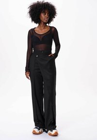 Zwarte lichtgewicht mesh long-sleeve top met een lage halslijn, gecombineerd met hoge zwarte brede broekspijpen. Opvallende knoopdetails op de broek.