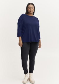 Tengerész navy oversized kötött felső háromnegyedes ujjakkal, fekete, testhezálló nadrággal és krém színű bokacsizmával párosítva. Egyszerű dizájn és sima textúra.