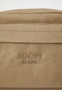 Borsa in tela beige con superficie texturizzata, cuciture sottili e logo "JOOP! JEANS" impresso sul pannello frontale.