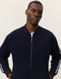 Ναυτικό φούτερ με φερμουάρ και λευκές ρίγες στα μανίκια, διαθέτει ριμπ κολάρο και πλαϊνές τσέπες. Απαλή ύφη με διακριτική επωνυμία στο στήθος.