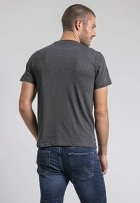 T-shirt en coton gris avec un col rond et des manches courtes, vue de dos. Associée à un jean en denim bleu. Design simple et décontracté.