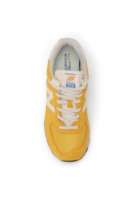 Yellow New Balance 574 sneaker featuring mesh and suede materials, white accents, and a textured sole with a lace-up closure.