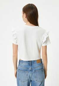 Hvid kortærmet bluse med flæser ved ærmerne, tekstureret stof, cropped længde, kombineret med højtaljede lyseblå jeans.