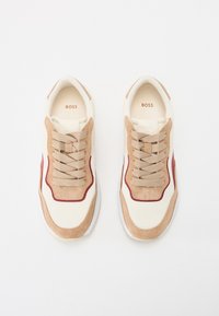 Tan ja kreem värvi sneakersid, mis on valmistatud võrgust ja nahast. Omab beeži paelu, punaseid detaile ja valget talda. "BOSS" logo sisetallal.