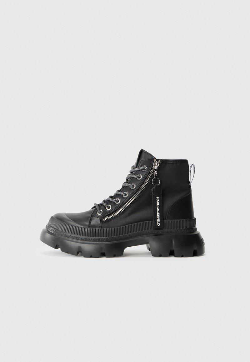 Zwarte enkelboots met een glanzende afwerking, rubberen zool, veter-sluiting en een rits aan de zijkant. Voorzien van een merklabel en textuurdetails langs de zool.