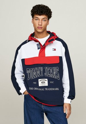 Cazadora con bloques de color en azul marino, blanco y rojo, con capucha. Presenta un gran estampado gráfico y un bolsillo frontal. Confeccionada en tejido ligero y texturizado.