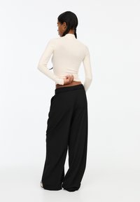 Langärmliger cremefarbener Rollkragenpullover, kombiniert mit schwarzen weiten Hosen, die eine glatte Stoffstruktur und einen lockeren Sitz in der Taille zeigen.