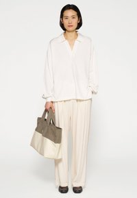 Witte langemouw overhemd met een kraag, gecombineerd met lichtbeige broek en een twee-kleurige totebag in grijs en room. Zachte texturen en een losse pasvorm.