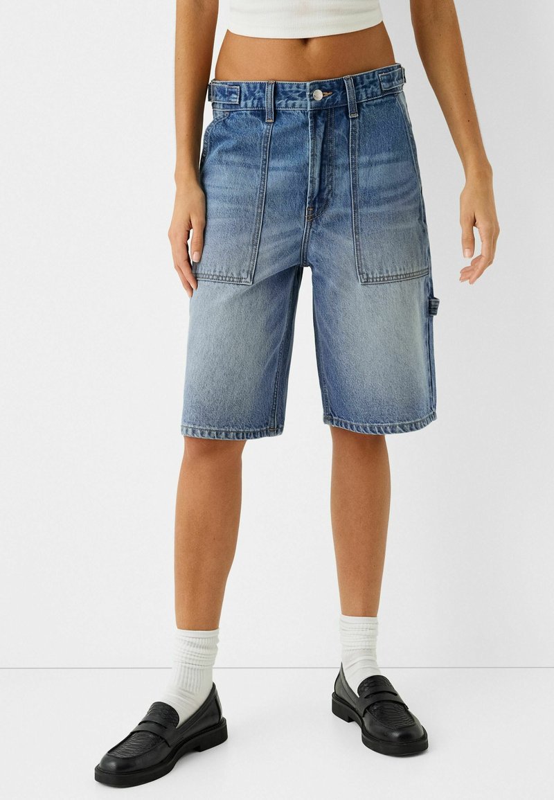 Lichtblauwe denim bermuda shorts met een losse pasvorm, twee voorzakken en een riemlus. Gecombineerd met zwarte instappers en witte sokken.