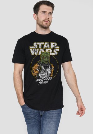 Man wearing black Star Wars t-shirt featuring a green alien bounty hunter with text "Bounty Hunter for Hire," paired with blue jeans.
