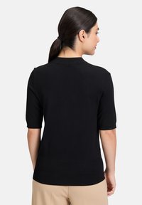 Maglione nero a maniche corte con scollatura rotonda, silhouette aderente e orlo a coste. Il tessuto appare liscio con dettagli minimi.