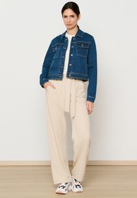 Tamsiai mėlynas džinsinis švarkas su sidabriniais mygtukais, dviem krūtinės kišenėmis, derinamas su šviesiai rudomis plačiomis kelnėmis ir raštuotais sportbačiais. Švelnūs tekstūros.