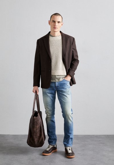 Brown pinstripe blazer over a light knitted sweater, paired with faded blue jeans and dark sneakers, holding a brown leather tote bag.