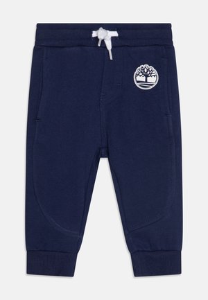 Jogging bleu marine pour tout-petit avec taille et poignets côtelés, cordon blanc, poches latérales et logo arbre blanc sur la cuisse droite.