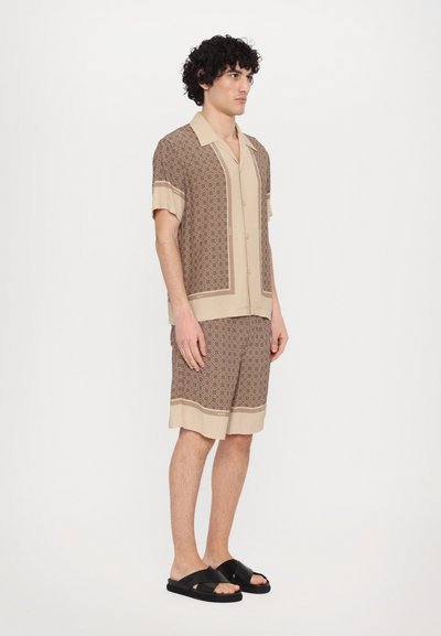 Ensemble de chemise à manches courtes et de shorts avec un motif géométrique marron et des accents beiges ; associé à des sandales à glissière noires.