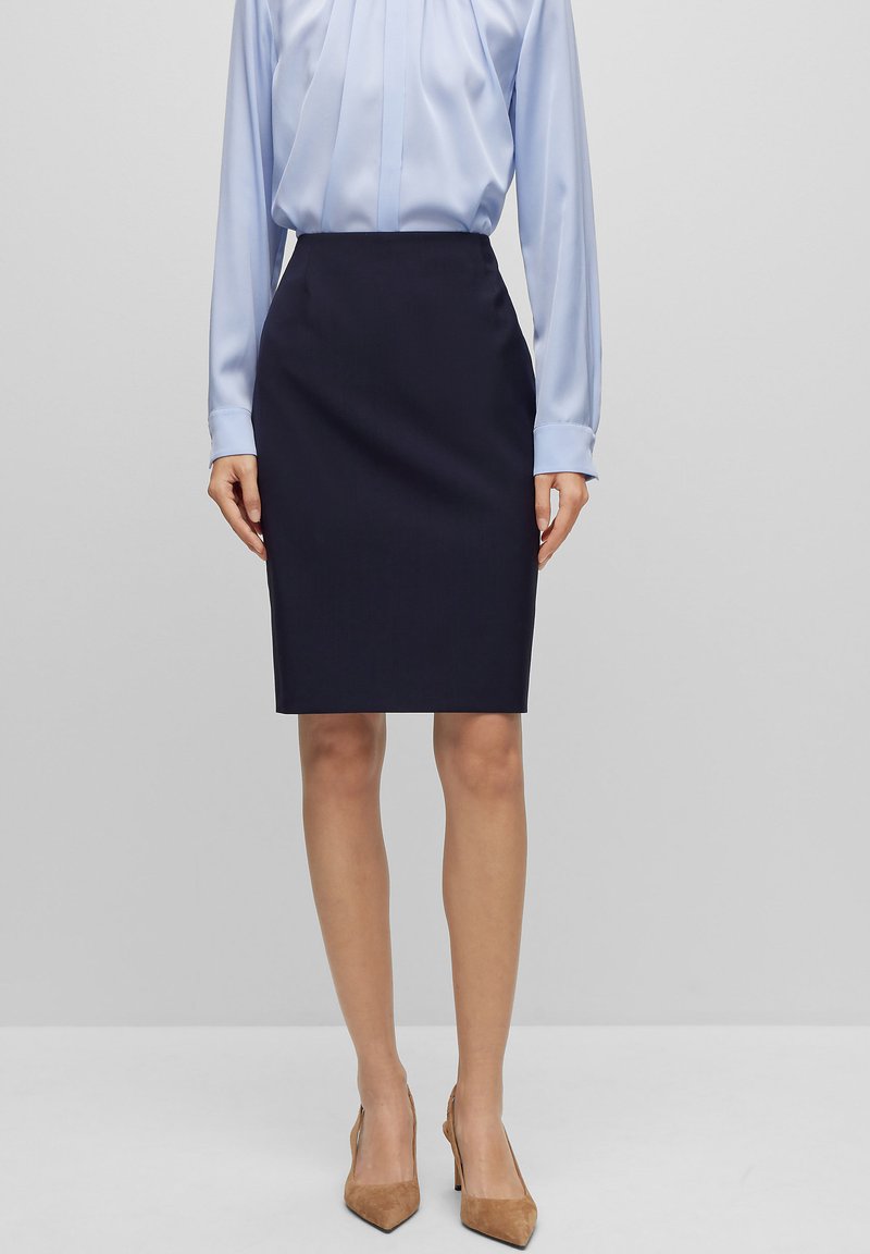 Jupe crayon marine au design ajusté, fabriquée dans un tissu lisse, associée à un chemisier en satin bleu clair, complétée par des talons beiges.