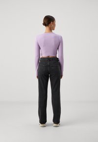 Purple ribbed long-sleeve crop top paired with high-waisted black straight-leg jeans. Flat shoes, minimal detailing on garments.