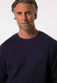 Marinblå långärmad tröja i våfflad textur med rund hals och präglad logotyp på bröstet. Mjuk kvalitet och avslappnad passform.