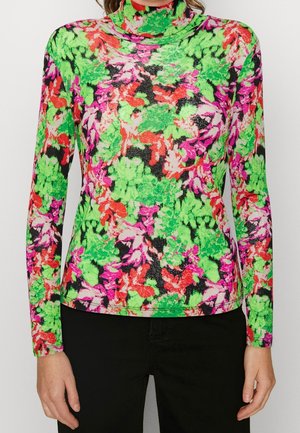 Chemise à manches longues col roulé avec motif floral abstrait vert vif, rouge, rose et noir portée avec un pantalon noir.