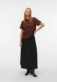 Bordowy top z krótkim rękawem o luźnym kroju, zestawiony z lejącą się czarną spódnicą maxi. Modelka nosi czarne botki. Prosty design, miękka faktura.