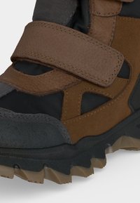 Gros plan d'une chaussure de randonnée marron et noire avec une bride Velcro et une semelle beige et noire robuste pour une utilisation en extérieur.
