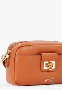 Borsa cosmetica in pelle marrone con dettagli in oro, forma rettangolare, chiusura con cerniera superiore e un gancio decorativo. Presenta il logo del marchio, V*73.