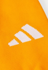 Gul textil med en vit logotyp i tre ränder. Tyget har ett strukturerat stickat mönster som framhäver den klara färgen och logotypdesignen.