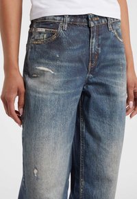 Denim jeans in een vervaagde blauwe kleur, met een relaxte pasvorm, versleten details en een klassieke vijf-zakken ontwerp met zichtbare stiksels.
