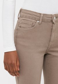 Beige denim jeans med en tettsittende design, fem lommer og metallbeslag. Livbåndet har en beltestrop for justerbar passform.