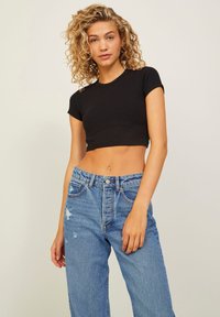 Top corto a coste nero con maniche corte abbinato a jeans in denim blu strappati a vita alta. Presenta una chiusura con bottone e cerniera.