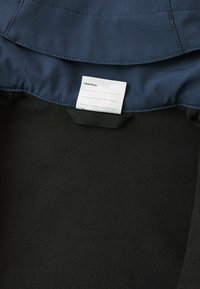 Innenfutter einer marineblauen Jacke mit schwarzem Fleece. Ein weißes Etikett mit der Aufschrift "Ich war hier:" gefolgt von leeren Zeilen zum Ausfüllen von Informationen.