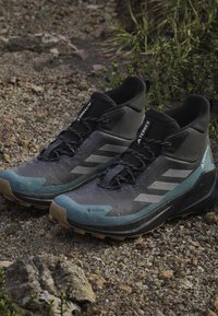 Zapatillas de trail con un diseño en negro y gris, material GORE-TEX, parte superior texturizada y suela de goma con patrones de taquilla visibles.