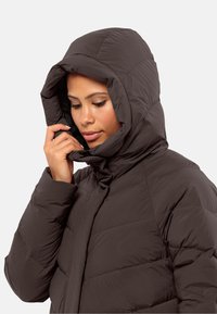 Bruine pufferjack met een capuchon, met een gequilte ontwerp en een hoge kraag. De stof lijkt glad en een beetje glanzend.