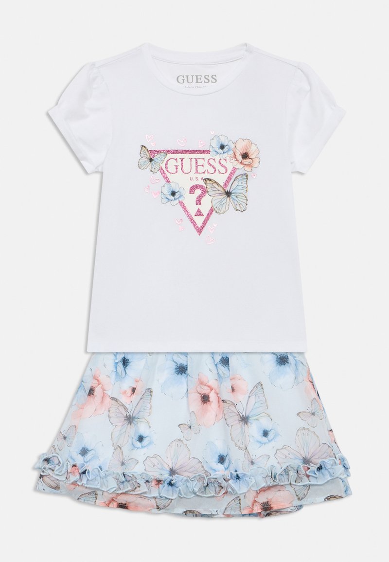 Λευκό κοντομάνικο πουκάμισο με λαμπερό λογότυπο "GUESS" και λουλουδάτο μοτίβο με πεταλούδες. Συνδυασμένο με μια ανοιχτό μπλε, βολάν φούστα με λουλουδάτο σχέδιο.