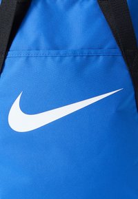 Μπλε υφασμάτινο σακίδιο πλάτης με μεγάλο λευκό λογότυπο Nike swoosh. Επιφάνεια με υφή, μαύρα λουριά και φερμουάρ σε μπροστινή τσέπη.