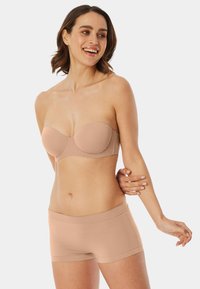 Strapless naadloze nude beha met gladde, gewatteerde cups en een naadloos ontwerp, gecombineerd met bijpassende naadloze nude boyshorts met een zachte textuur.