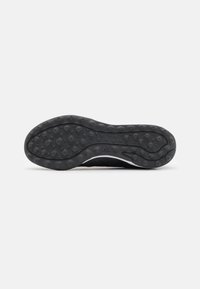 Suola di scarpa sportiva nera in gomma testurizzata, con motivi di presa circolari, bordi leggermente curvi e un design del battistrada distintivo.
