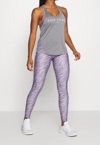 Gray athletic tank top with "PINK SODA" logo, paired with purple and gray tiger-striped leggings. White athletic shoes.