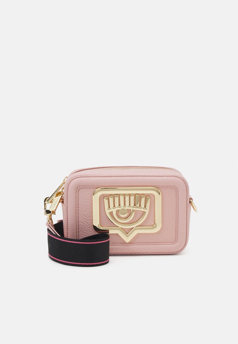 Borsa a tracolla in pelle rosa con un evidente dettaglio in metallo a forma di occhio dorato, superficie texturizzata e una tracolla nera con accenti rosa.