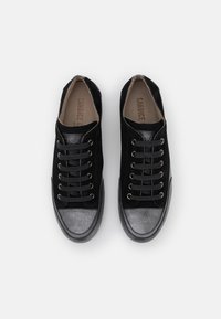 Ett par svarta sneakers med grå tåkuvar och svarta snören, sedd ovanifrån mot en vit bakgrund.