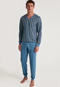 Blauw-wit geruite shirt met lange mouwen en V-hals, gecombineerd met effen blauwe joggingbroek; katoenen stof, relaxte pasvorm, ribgebreide boorden bij de polsen en enkels.