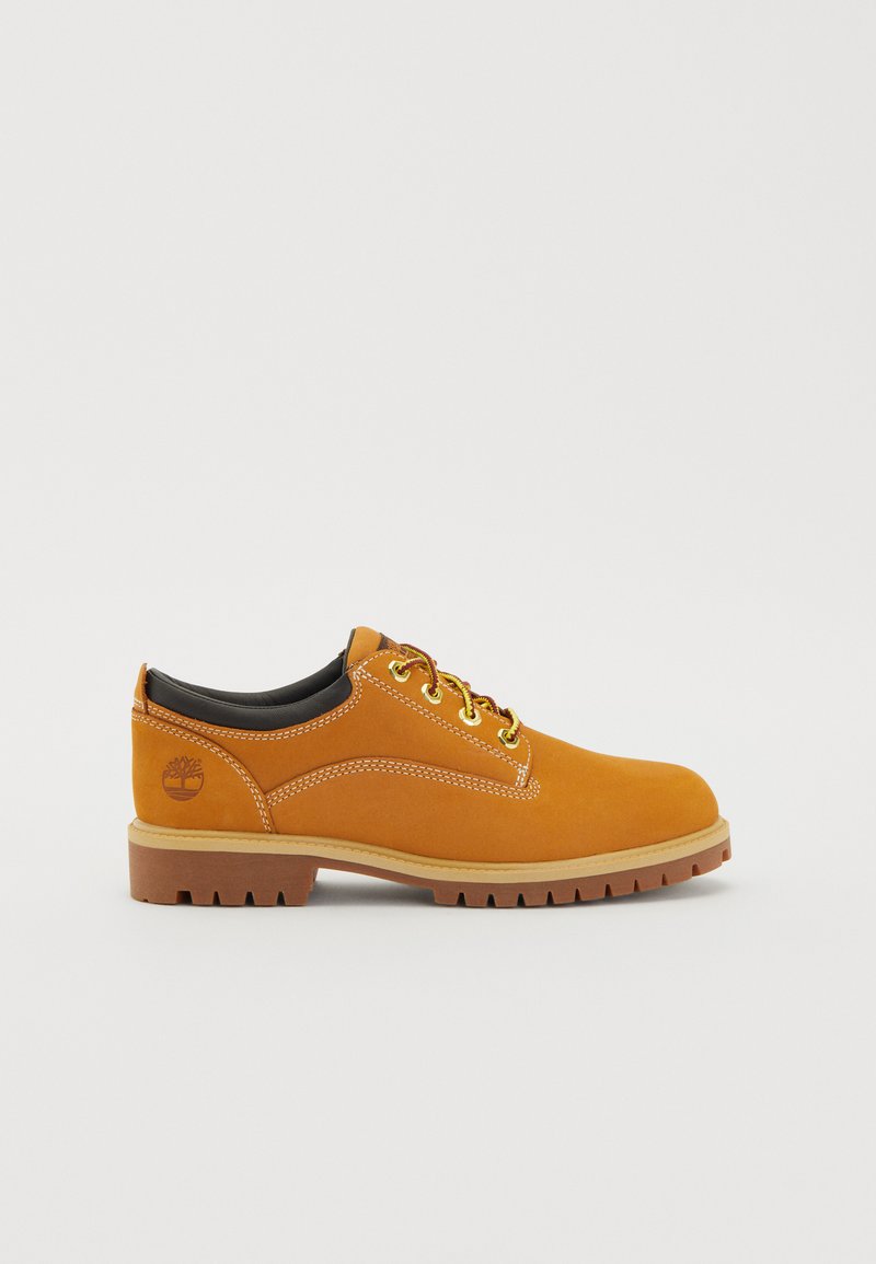 Tan leather shoes with a round toe and black lining. Features yellow laces and contrasting white stitching. Light brown rubber sole with tread.