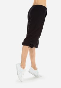 Pantaloni neri cropped realizzati in tessuto morbido con risvolto, dotati di tasche laterali e vita elastica, abbinati a sneakers bianche.
