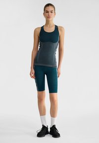 Teal sportieve tanktop met een textuurpatroon en bijpassende shorts, voorzien van zwarte accenten en grijze zijdetails. Zwarte sneakers en witte sokken.