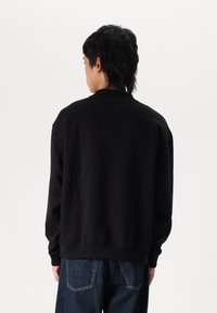 Schwarzer Sweatshirt mit Rundhalsausschnitt, langen Ärmeln und gerippten Bündchen. Hat eine lockere Passform und sichtbare Nähte am Saum und an den Nähten.