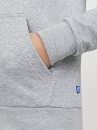 Felpa grigia con polsini a costine, dotata di tasca a marsupio. Etichetta blu distintiva sulla tasca. Tessuto liscio e strutturato.