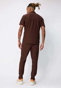 Chemise marron à manches courtes et pantalon assorti en tissu lisse, avec un col classique, une coupe décontractée et un motif texturé subtil.