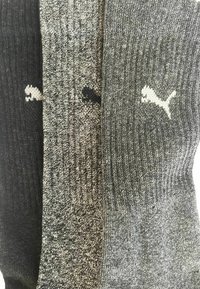 Drei Paare Socken in unterschiedlichen Schwarz- und Grautönen, mit einem gestrickten Muster und Puma-Logos in kontrastierenden Farben auf jedem Paar.