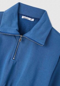 Maglione blu realizzato in morbido cotone con colletto con zip. Presenta una texture liscia e un'etichetta che indica la taglia "S" di Terranova.
