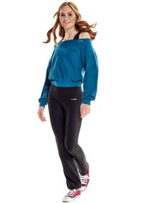 Teal off-shoulder sweatshirt and black leggings with logo accents; paired with red sneakers. Smooth fabric, relaxed fit, and elastic waist.